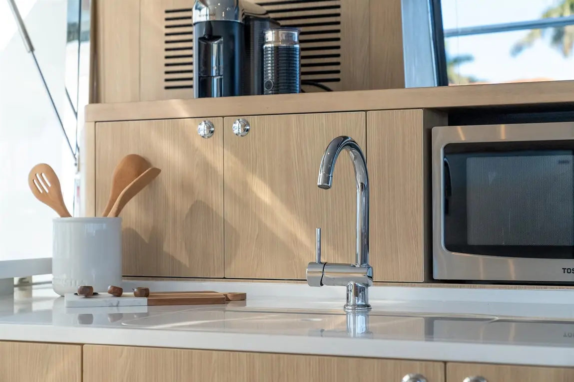 Modern kitchen with a chrome tap, wooden utensils in a container, and a microwave against a wooden cabinet backdrop.
